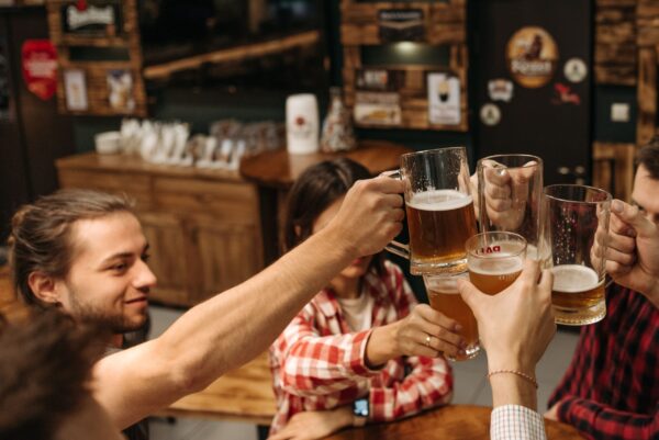 Friends celebrate with a toast using beer mugs in a cozy indoor setting.