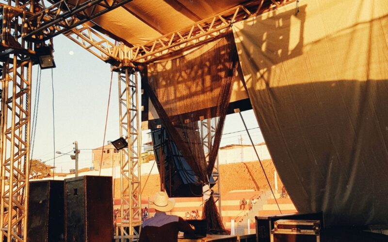 A man sets up equipment on stage with dramatic lighting at sunset.