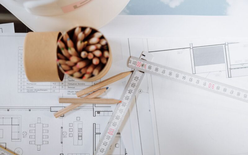 Colorful pencils and ruler atop architectural blueprints on a workspace.
